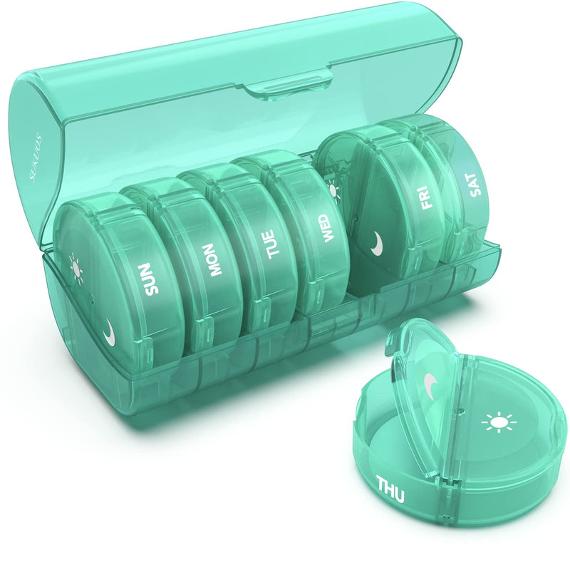 a green plastic pill box with a lid open with text: 'SUKUOS C SUN MON TUE THU WED FRI SAT'