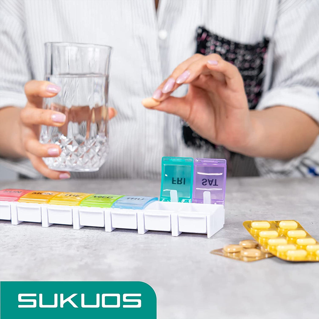 a hand holding a glass of water and a pill in a pill box with text: 'THU SUKUOS'