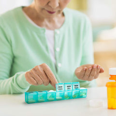 a person holding a pill box with text: 'MON TUE WED WEEK 2 WEEK 2 WEEK 2'