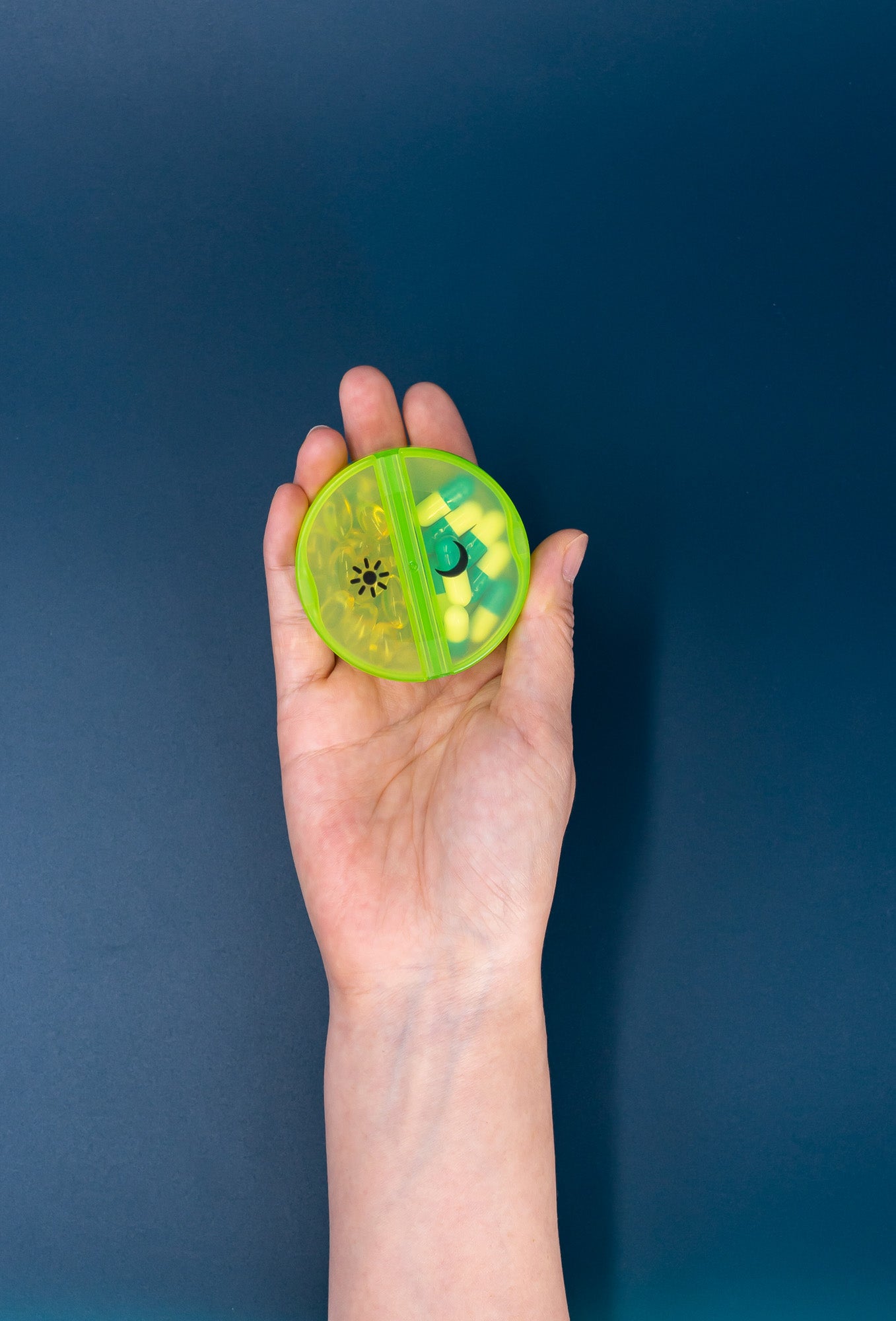 a hand holding a round green pill case 