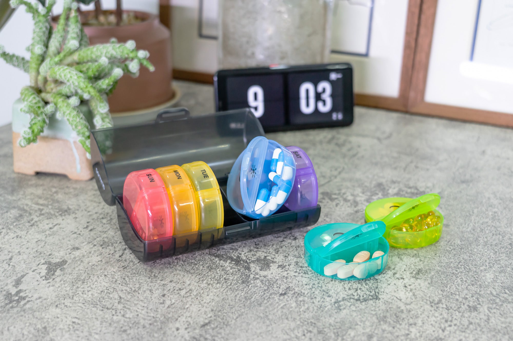 a black plastic container on a counter with round, rainbow pill compartments 